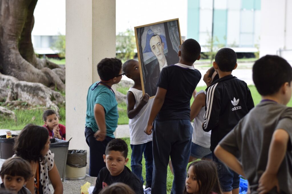Crianças seguram uma réplica do retrato de Murilo Mendes de Guignard.